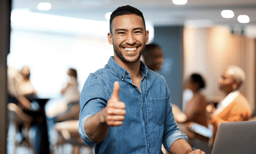 Shot of a young businessman showing thumbs up while using a laptop